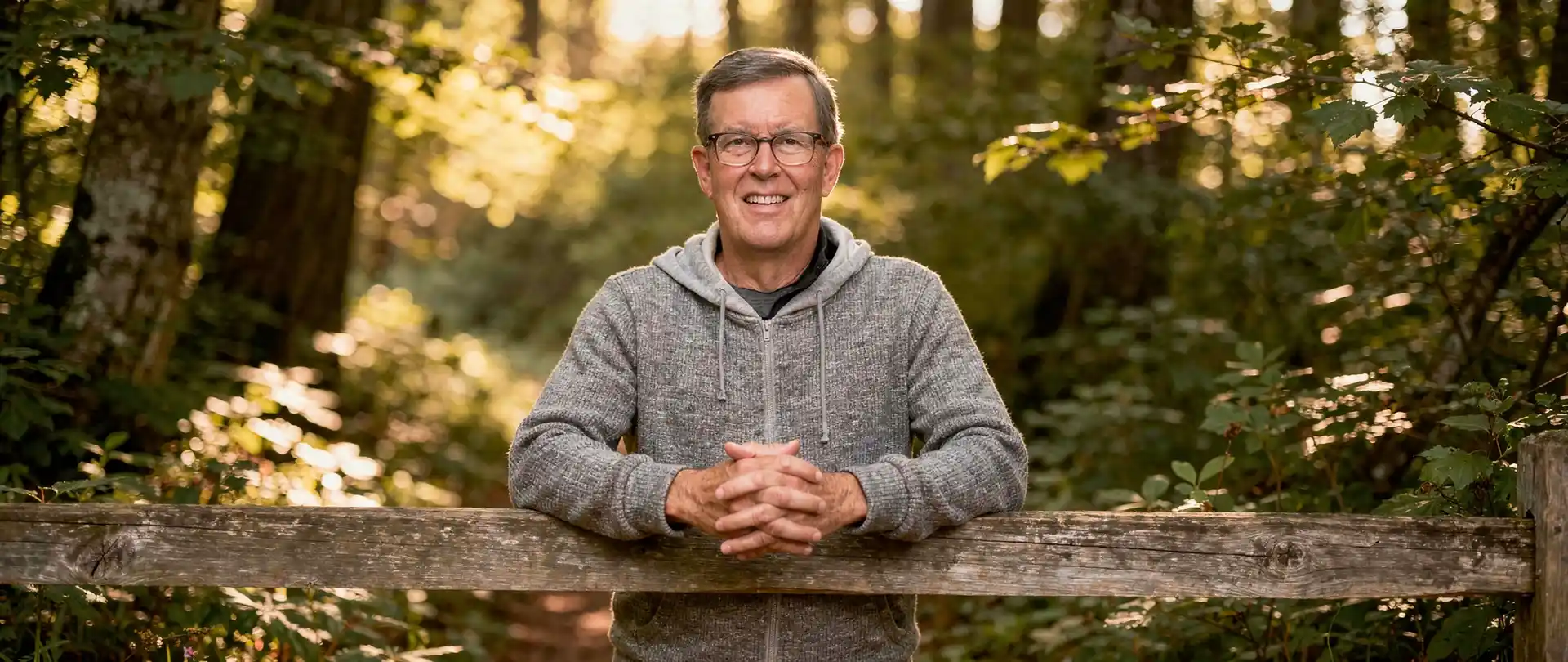 Image of Michael Christian leaning on split rail fence in a forest